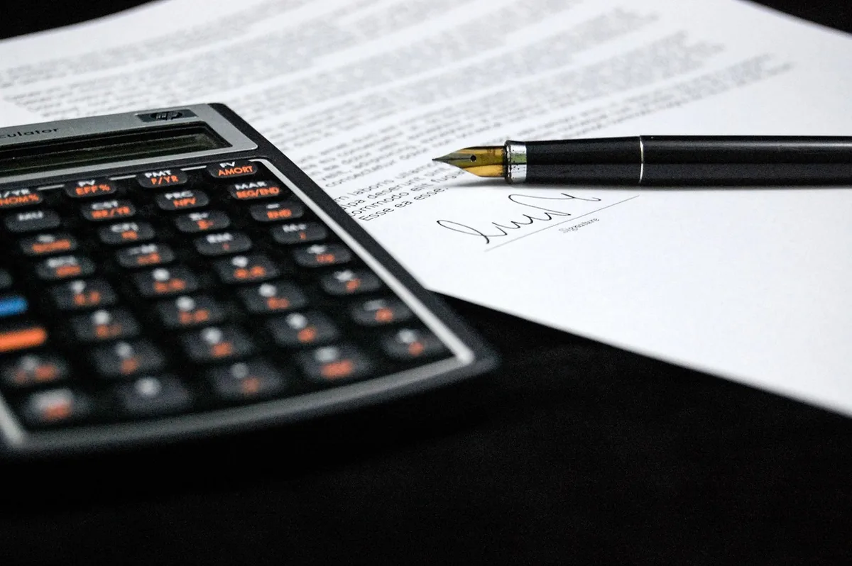 Deux mains anonymes pointant des documents de prêt et une calculatrice dans une salle lumineuse