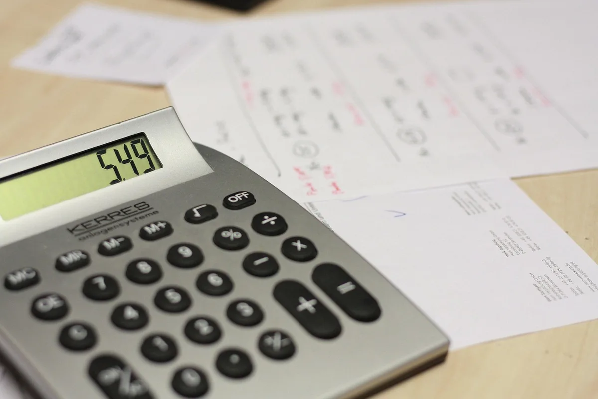 Calculatrice, carnet et documents de tarifs posés sur un bureau en lumière du jour